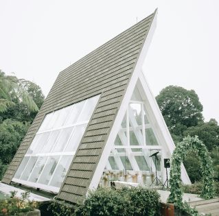 Exterior of contemporary geometric building with windows near green archway and plants near forest under cloudless sky in daytime in summer